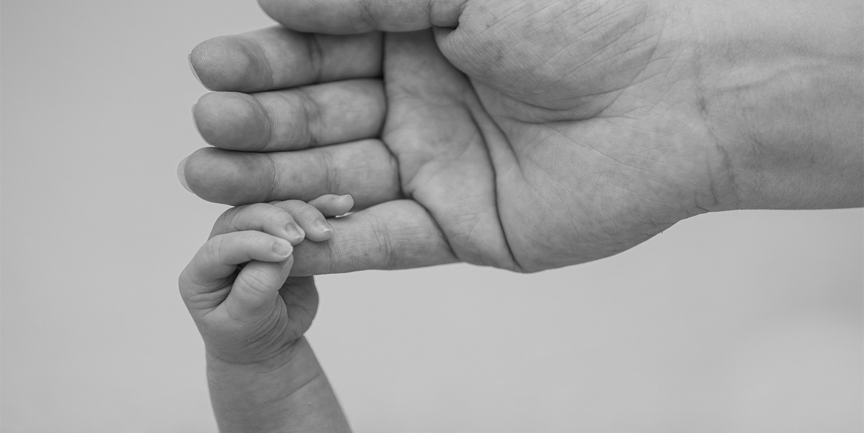 En bebishand håller om fingret på en vuxenhand.